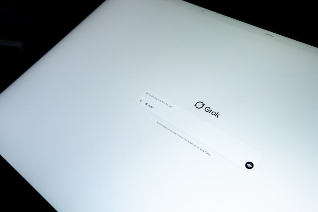 Angled photo of a computer screen displaying the Grok AI interface with a search bar, captured in a bright minimal setting.